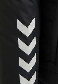 Pantaloni sportivi neri con un tessuto a trama, caratterizzati da ampi motivi a zig-zag bianchi che si estendono lungo il lato per visibilità e contrasto di design.