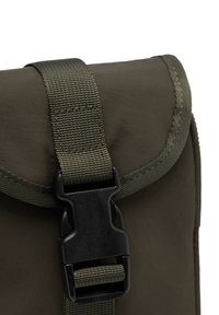 Khaki seljakott, mille klapp on musta plastist kinnitusega, valmistatud vastupidavast riidest ja õmmeldud servadega. Ülemisel osal on nähtav tekstureeritud rihm.