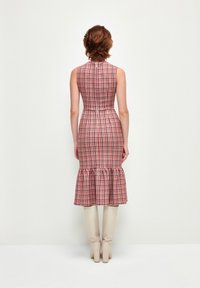 Ruudullinen midi-mekko punaisena ja valkoisena, tiukka yläosa, röyhelöhelma, kangas näyttää tekstuurilta. Yhdistetty polvimittaisiin beigeihin saappaisiin.