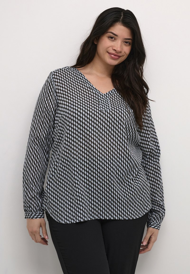 Long-sleeve, V-neck blouse featuring a black and white diamond pattern, semi-sheer fabric, and a relaxed fit. Paired with black pants.