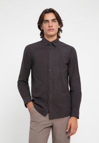 Sötét kockás ing, gombos gallérral, hosszú ujjakkal és kék gombokkal. Az anyag sima textúrájú, testre szabott kialakítással.