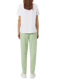Weißes Baumwoll-T-Shirt und hellgrüne Sweatpants. Die Hose hat einen elastischen Bund und ist an den Knöcheln leicht tapered. Schlichtes Design.