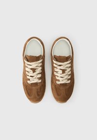 Brown suede sneakers with cream laces, featuring a rounded toe, textured side panels, and a white inner lining. No visible logos.