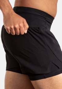 Zwarte sportshorts van een textuurstof, met een elastische tailleband en zijzakken, ontworpen voor comfort en bewegingsvrijheid tijdens trainingen.