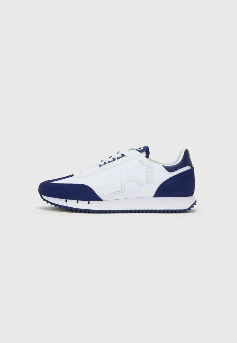 White and navy athletic shoes with a textured upper, lace-up design, and rubber sole featuring distinct multi-directional tread pattern.