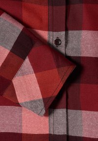 Manche de chemise à carreaux rouges et noirs repliée sur le devant avec un bouton noir visible sur le poignet.