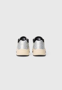Zapatillas deportivas plateadas con un upper texturizado, acentos negros y una suela beige. Presentan paneles de malla para ventilación y una puntera redondeada.