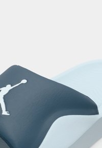 Σκούρα μπλε σαγιονάρα με υφασμάτινο επάνω μέρος, που διαθέτει λευκό λογότυπο. Ελαφριά σχεδίαση με μαλακή ελαφριά μπλε σόλα και καμπυλωτό σχήμα.