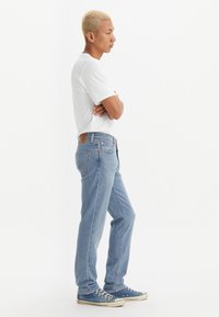 Lyseblå denimjeans med rett passform, med en brun lærlapp, fem lommer og sølvmetallbeslag. Brukt med en hvit t-skjorte.