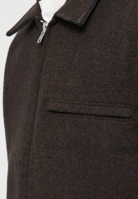 Braune Wolljacke mit strukturierter Oberfläche, ausgestattet mit Kragen, durchgehendem Reißverschluss vorne und einer einzelnen Brusttasche.