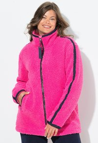 Pehmeä vaaleanpunainen fleece-takki, jossa on korkea kaulus, tummansiniset sivuviivat, edessä vetoketju ja kaksi sivutaskua. Pehmeä rakenne ja rento istuvuus.