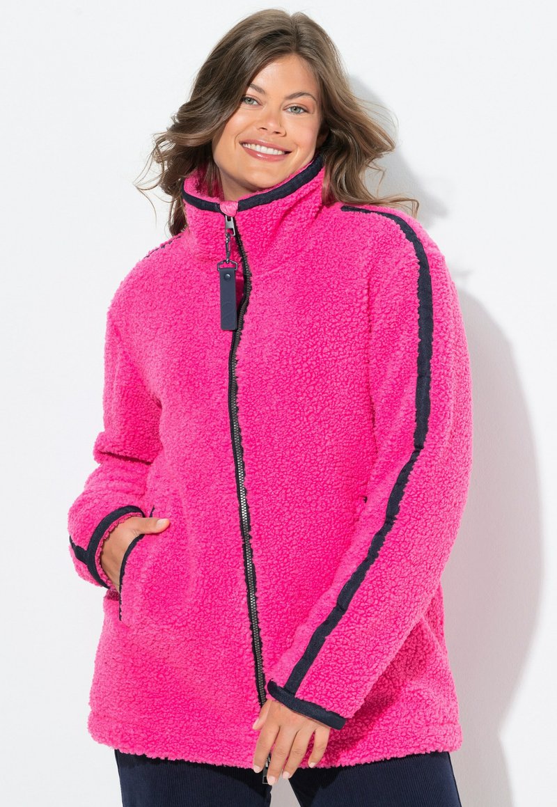 Pehmeä vaaleanpunainen fleece-takki, jossa on korkea kaulus, tummansiniset sivuviivat, edessä vetoketju ja kaksi sivutaskua. Pehmeä rakenne ja rento istuvuus.