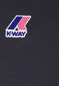 Tamno plavi materijal s rebrastom teksturom, na kojem se nalazi K-Way logo u plavoj, crvenoj i bijeloj boji. Logo uključuje koso postavljene pruge iznad teksta.