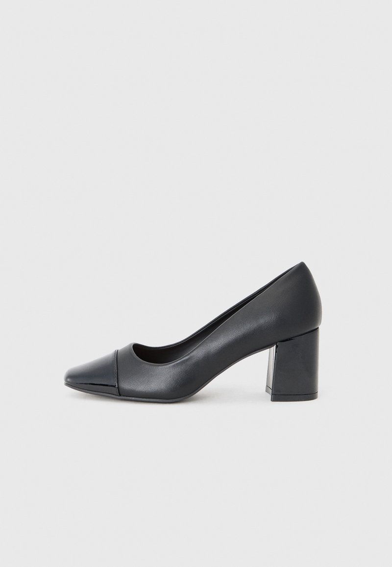 Chaussure femme en cuir noir à talon bloc avec embout arrondi sur fond gris clair.