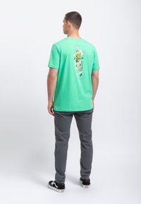 Lichtgroen katoenen t-shirt met een grafische print van een spelconsole op de achterkant. Het shirt heeft een relaxte pasvorm en korte mouwen.