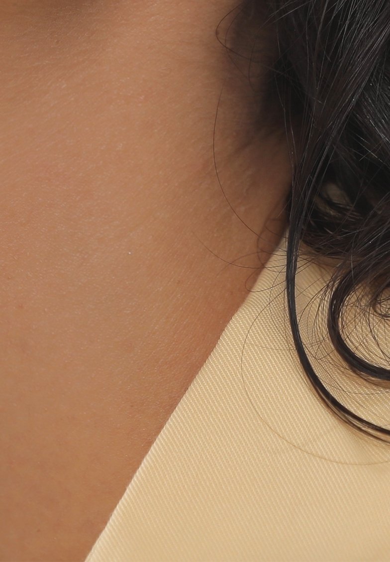Gros plan sur le cou d'une personne et ses cheveux foncés contre un tissu beige à motif texturé.