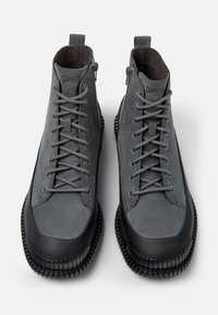 Zapatillas altas grises con parte superior de cuero liso y suela de goma. Presentan cordones y cremallera lateral para el cierre. Acabados de goma texturizada en la suela.