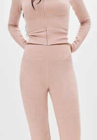 Set di pigiama lavorato a maglia in rosa chiaro, composto da una maglietta aderente a maniche lunghe a coste e leggings a vita alta e a coste. Texture morbida, dettagli minimi.