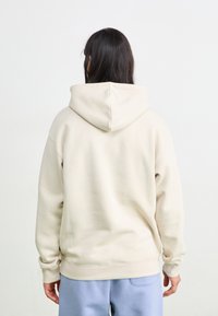 Hoodie aus hellbeigem Stoff mit lockerer Passform, gerippten Bündchen und einem schlichten Design ohne sichtbare Grafiken oder Muster.