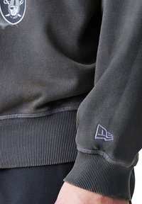 Temno siva trenirka z rebrastimi manšeti. Ima vezenje logotipa na prsih in majhen logotip na desnem rokavu. Mehka tekstura.
