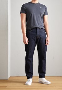 Šedé bavlněné tričko s krátkými rukávy, doplněné tmavě modrými džínami. Bílá plátěná teniska dokončuje outfit. Jednoduchý design, bez vzorů.