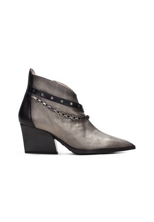 Stivale alla caviglia metallico argento e nero con punta appuntita, pelle martellata e una catena decorativa con borchie rotonde. Tacco basso a blocco.