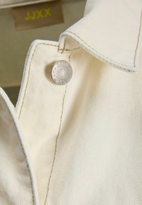 Γιακάς τζιν μπουφάν σε κρεμ απόχρωση με ορατή ραφή και μεταλλικό κουμπί χαραγμένο με "JJXX" και αστέρια.