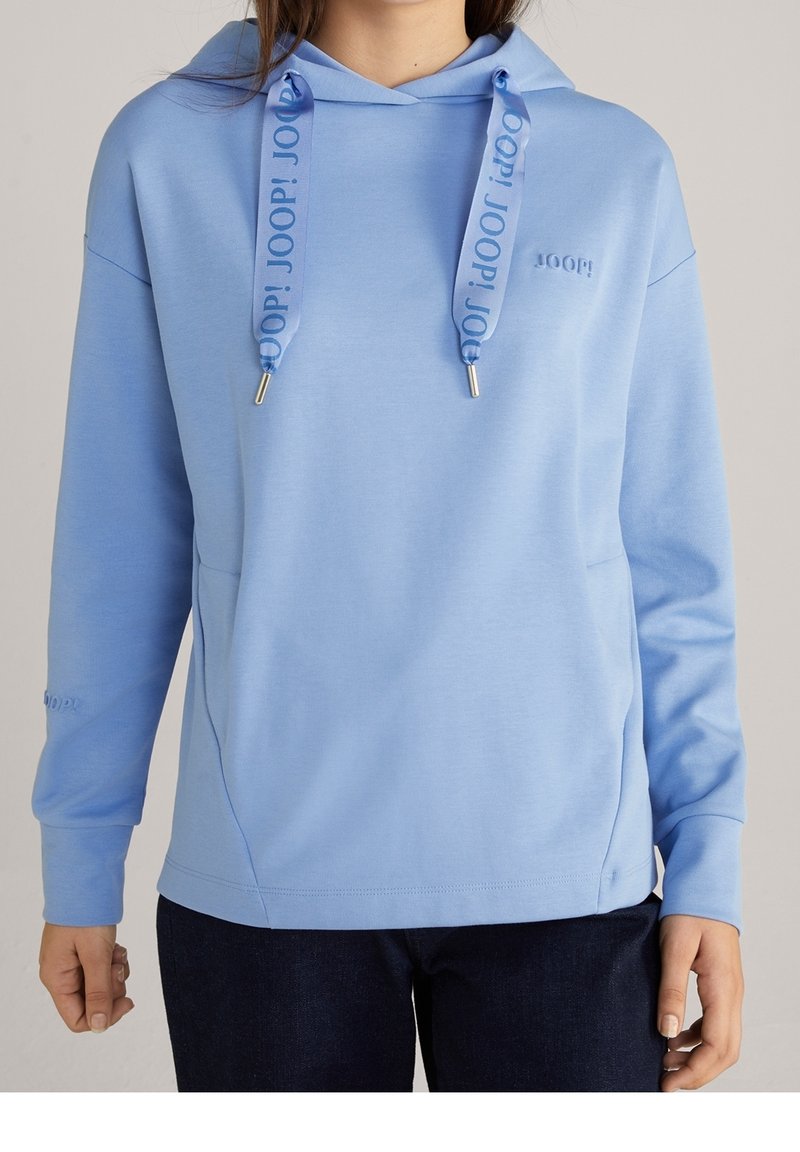 Sudadera con capucha azul claro, con textura suave, gran bolsillo frontal y cordones con estampado. El logo de la marca está mostrado de forma sutil.
