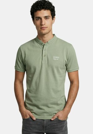 Homme portant un polo henley à manches courtes vert clair avec le logo "Lee Cooper Originals", debout les mains dans les poches d'un jean gris foncé.