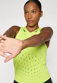 Canotta sportiva verde neon con design aderente, dotata di dettagli perforati per la ventilazione e di un logo Nike nero sul petto.