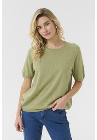 Tricou tricotat verde cu mânecă scurtă și guler rotund, cu detalii texturate tip bobble pe întreaga suprafață și o croială lejeră. Asortat cu blugi albaștri.
