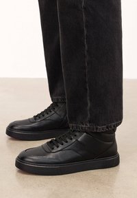 Mustad mustad sneakers on mustad nahast ja siledatest detailidest, ümmarguse varbaga ja kummist tallaga, millele on lisatud tumedad teksapüksid.