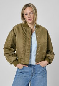 Olivgrüne Bomberjacke mit Reißverschluss, Druckknöpfen und gerippten Bündchen. Glatte Satinstruktur, kürzer geschnittenes Design und oversized Passform.