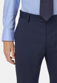 Mornarsko modri krojeni hlače z teksturirano površino. Imajo pas z zankami, zapirajo se na gumb in imajo stranske žepke; oblečene z svetlo modro karirasto srajco.