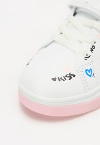 Fehér sneaker rózsaszín talppal, játékos graffiti-stílusú mintákkal fekete, kék és rózsaszín színekben, beleértve a szöveget és csillag díszítéseket.