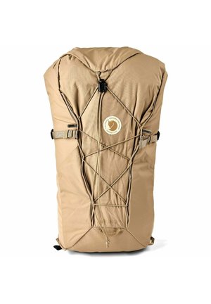 Beiger Wanderrucksack mit vorderen elastischen Schnüren, verstellbaren Seitenträgern, oberer Klappe und rundem Logopatch in der Mitte des Vorderteils.