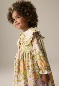 Blumenkleid in grünen, gelben und rosa Tönen mit Rüschekragen und Puffärmeln. Es hat große Blumen und eine geraffte Taille.