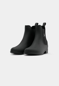 Botas de tornozelo pretas feitas de borracha, com uma textura suave, painéis laterais elásticos e puxadores para fácil calçado. Saltos quadrados e pontas arredondadas.