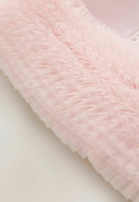 Różowa teksturowana tkanina z nałożonymi falbankami wykonanymi z przezroczystego tiulu, prezentująca miękki, delikatny wygląd. Krawędzie są starannie wykończone.