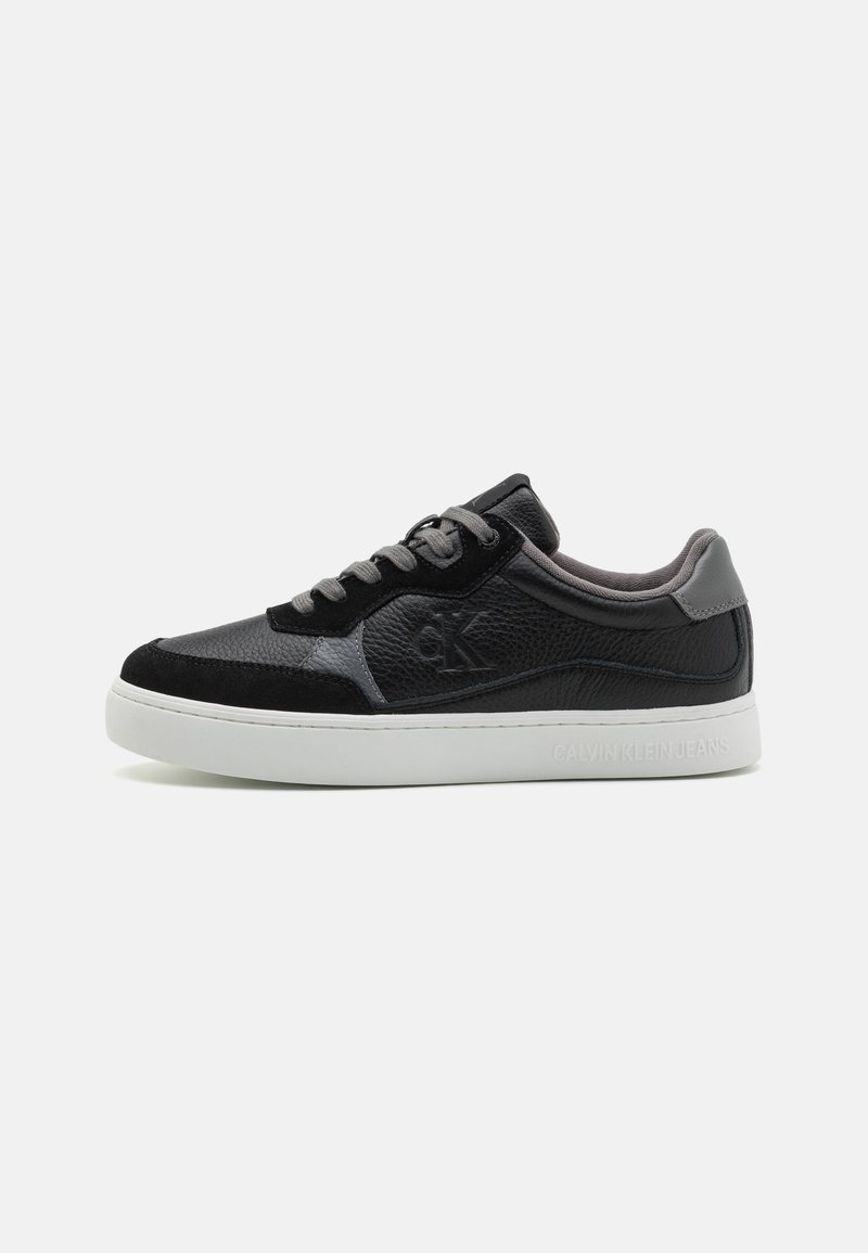 Black sneakers made of textured leather and suede, with gray accents, white sole, and lace-up design featuring a logo on the side.
