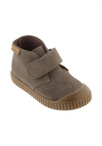 Botte chelsea en daim beige foncé avec une semelle en caoutchouc, dotée d'une large sangle en velcro et d'accents texturés.