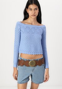 Ljusblå stickad off-shoulder kort tröja med ett strukturerat mönster, tillsammans med högmidjade denimshorts och ett brunt bälte med guldaccenter.