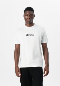 White cotton t-shirt with short sleeves, featuring black graphic text centered on the chest. Crew neck design, minimal texture.