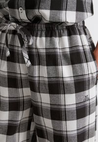 Schwarz-weiße Karohosen aus Flanell mit verstellbarem Bund und gesticktem Logo am Saum, aus einem weichen, strukturierten Stoff.
