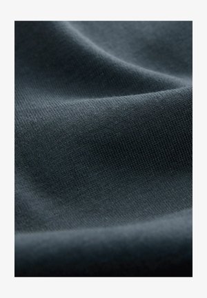 Dunkelgrauer Stoff mit glatter Textur, der ein engmaschiges Muster aufweist. Die Oberfläche wirkt weich, mit sanften Falten und subtilen Lichtreflexionen.