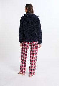 Marineblauer Fleece-Hoodie mit Herztextur, kombiniert mit rot-weißen Karohosen. Das Outfit hat eine Kapuze und einen legeren Schnitt.