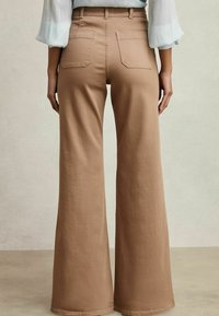 Beige High-Waist-Hosen mit weitem Bein aus glattem Stoff, ausgestattet mit zwei Gesäßtaschen und einer sauberen Nahtverarbeitung.