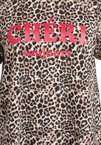 T-shirt con stampa leopardata in beige, marrone e nero, con testo rosso acceso che recita "CHÉRI toujours." Tessuto morbido con vestibilità rilassata.