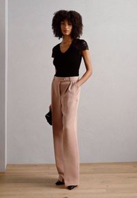Top negro con encaje, combinado con pantalones claros de talle alto y pierna ancha en color rosa. La modelo sostiene un pequeño bolso negro y lleva zapatos negros de punta.