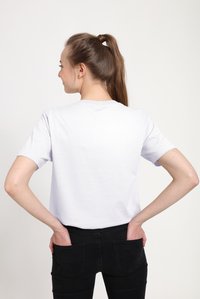 Camiseta blanca de manga corta vista desde atrás, con escote redondo y ajuste relajado, combinada con vaqueros negros. Diseño sencillo, sin patrones visibles.